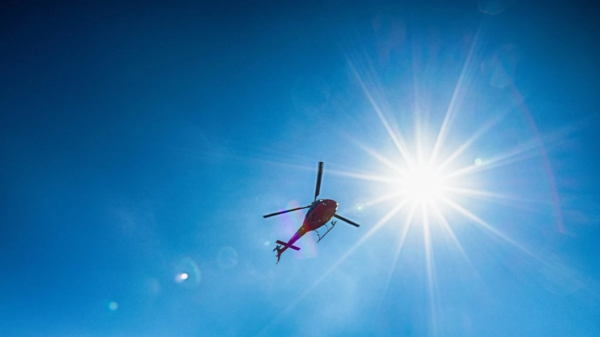 Helicopter in blue sky with bright sun above Shey Phoksundo Lake